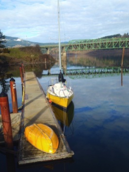 The yellow boat, the rusty dock stanchions, and the green bridge with grey cloud and blue sky reflections.